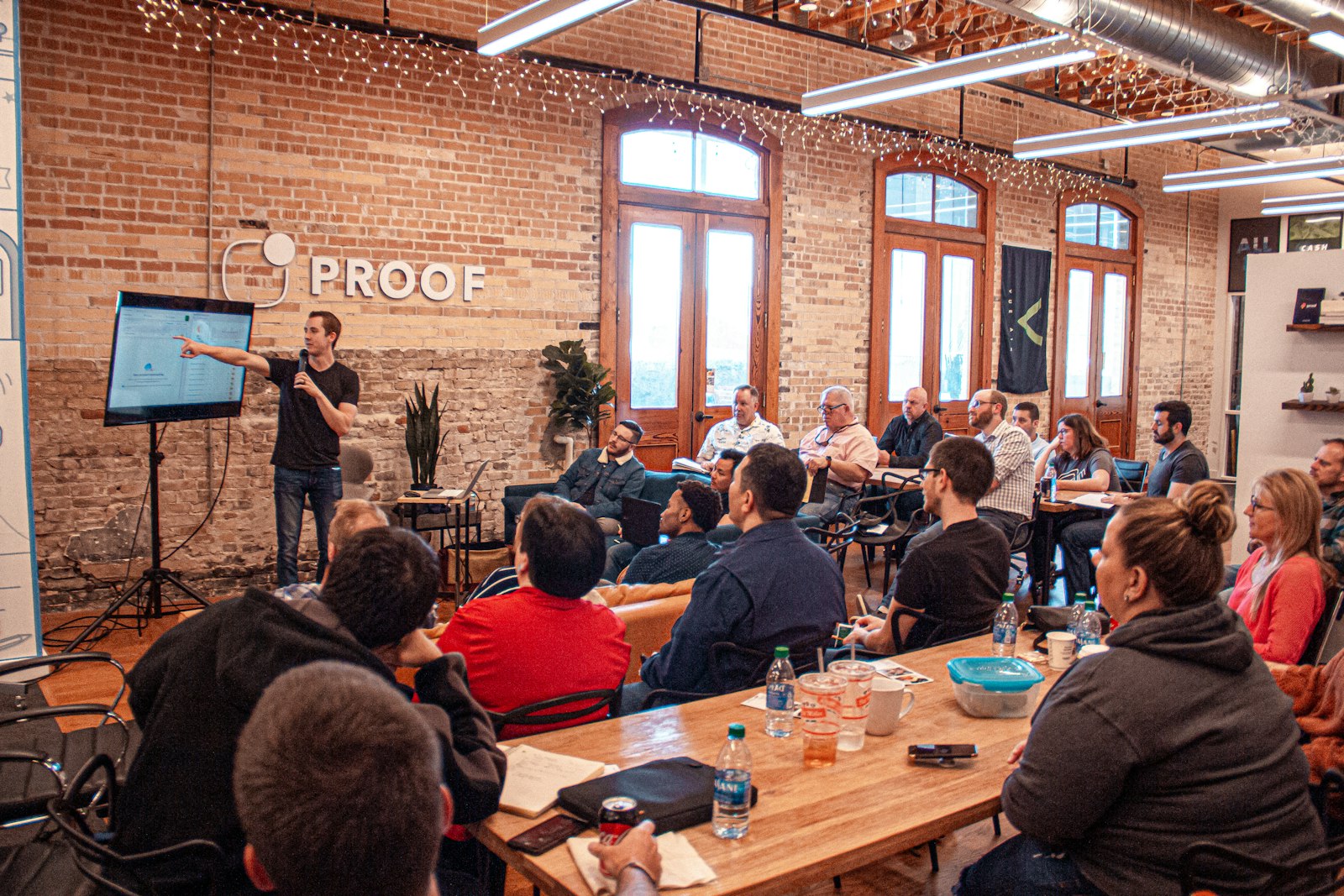 Speaker presenting to an audience at long tables in a brick-walled loft