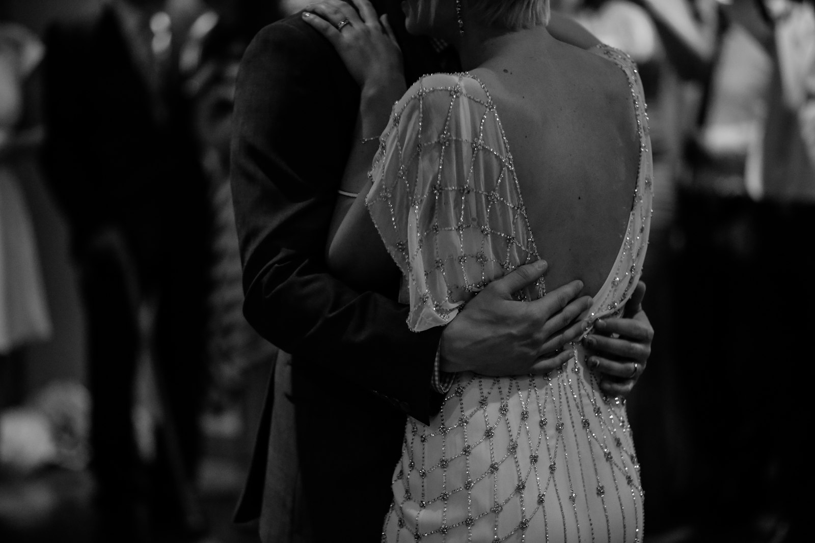 Bride in a beaded low-back gown and veil dancing with the groom, in monochrome
