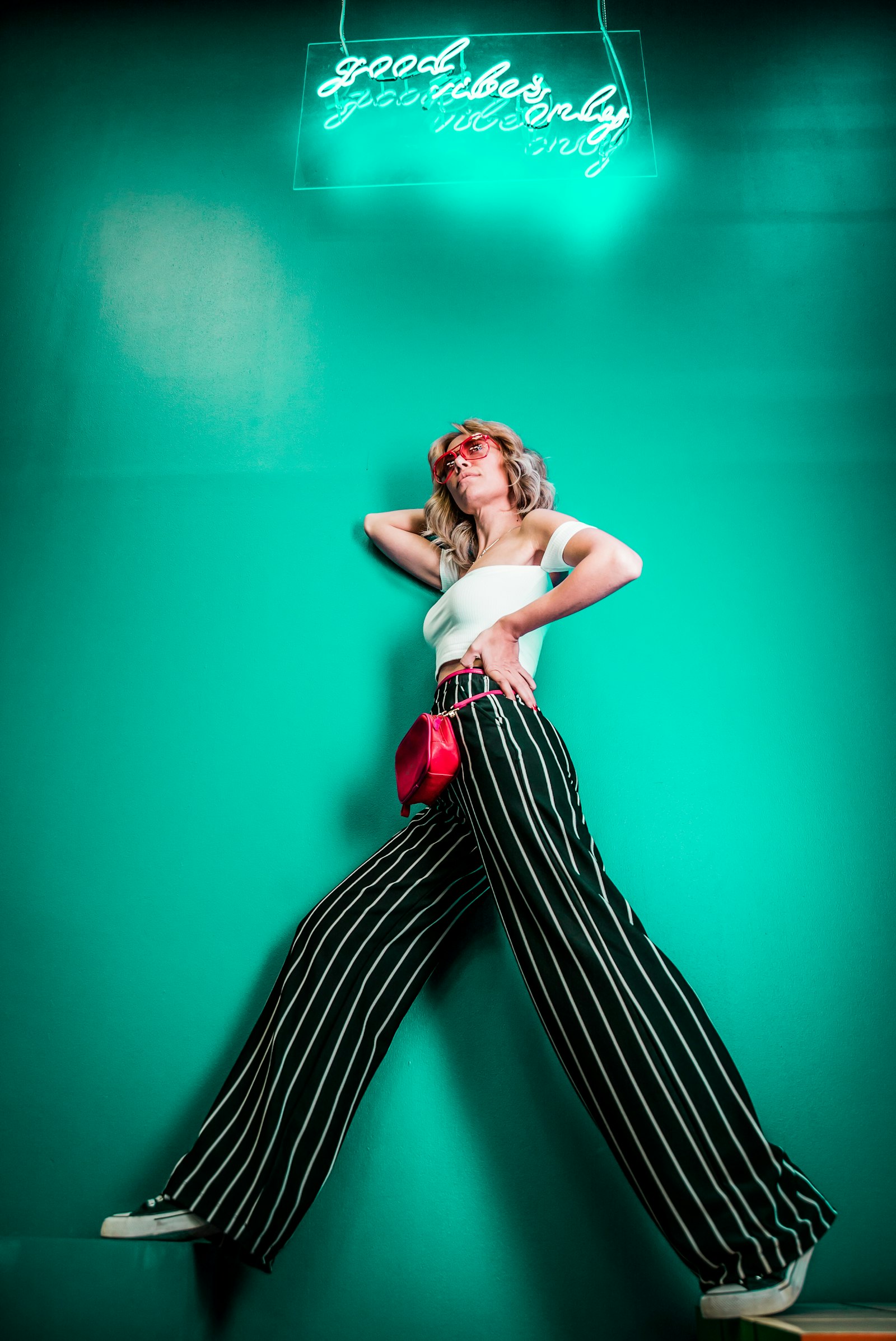 Woman posing under a neon sign on teal wall