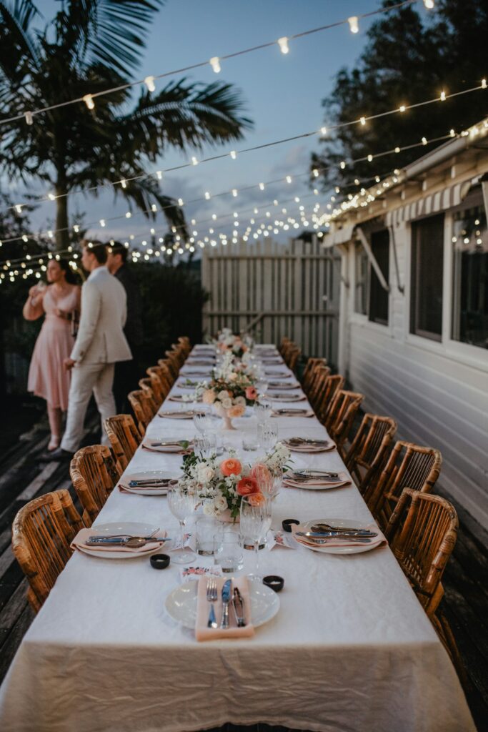 Long reception table under festoon lights at dusk with the couple at the far end